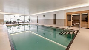 An indoor swimming pool with a clear view of the pool, a clock on the wall, and a seating area with chairs and potted plants. - 2 Bed in Woolacombe (oc-c29617) (Woolacombe)