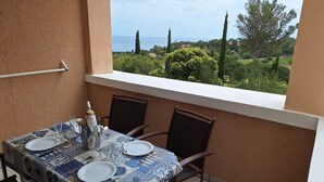 A balcony with a table set for two, overlooking a scenic landscape with trees and a view of the sea. - T2 apartment with sea view and private parking in Cap Esterel vacation village (Saint-Raphaël)
