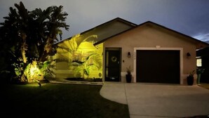 Een woonhuis met garage, een goed verlichte voortuin en een palmboom.