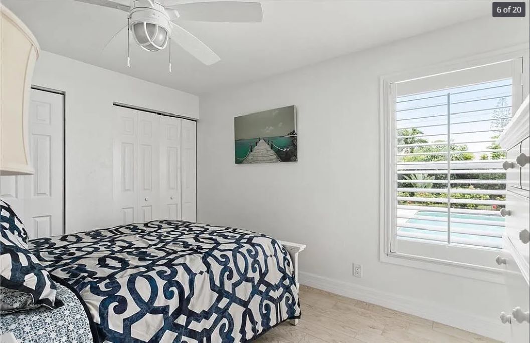 A bedroom with a bed, a ceiling fan, a window with blinds, and a painting on the wall.
