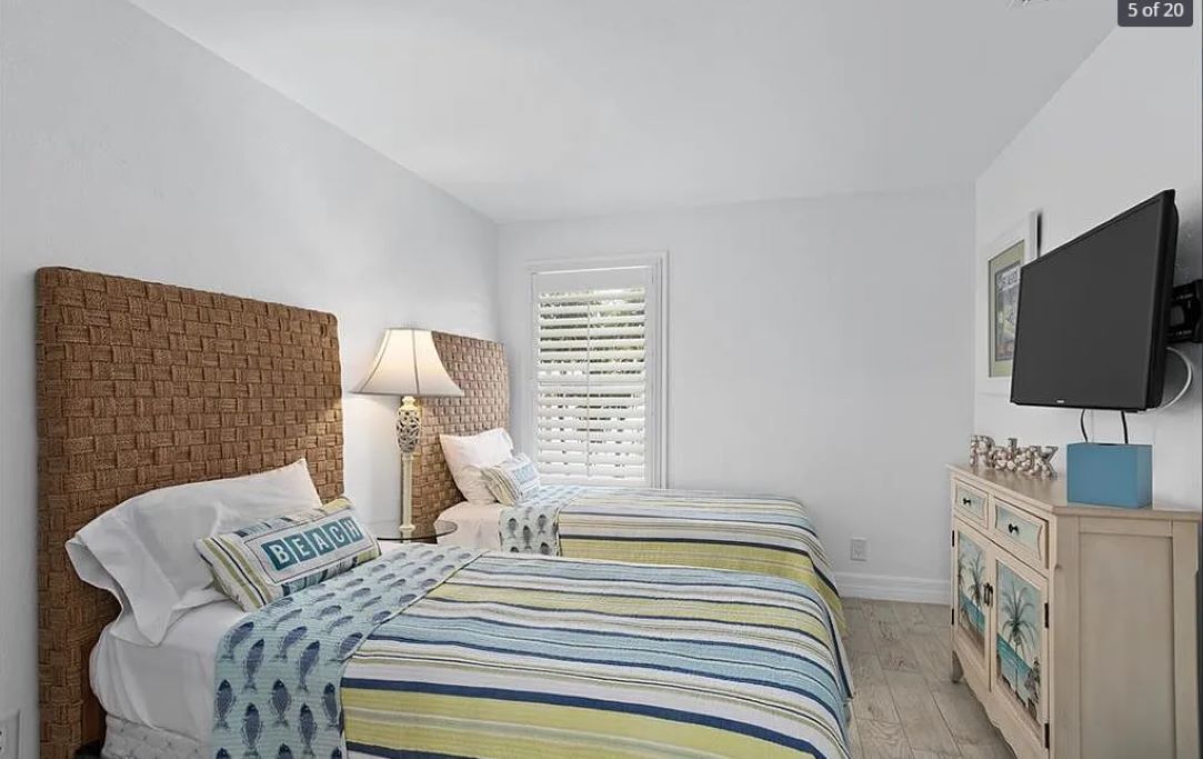 A bedroom with two beds, a brick headboard, a TV, a dresser, and a window with blinds.