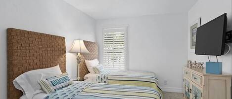 A bedroom with two beds, a brick headboard, a TV, a dresser, and a window with blinds.