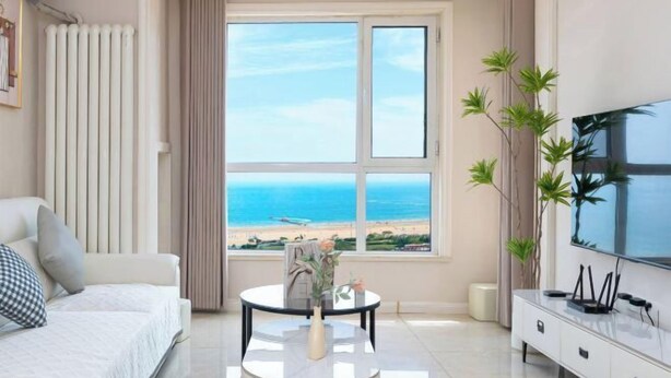 Een moderne hotelkamer met een groot raam met uitzicht op het strand, een bed, een televisie en een klein tafeltje met een vaas.