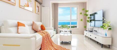 A modern living room with a sofa, coffee table, TV, and a view of the ocean.