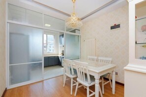 A room with a dining table and chairs, a chandelier, a sliding glass door, and a view of the city. - Qingdao Jinshatan Romantic Apartment (Qingdao)