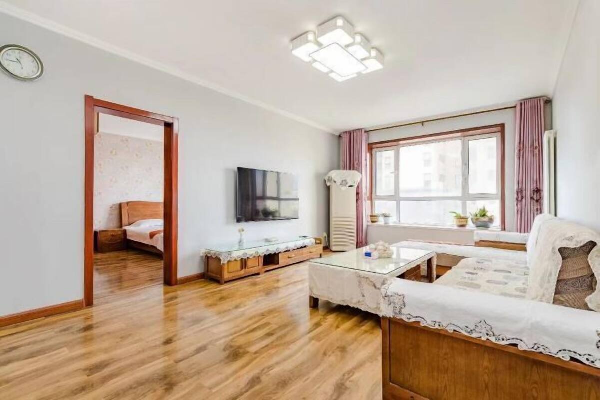 Ein Wohnzimmer mit Holzboden, einer Couch, einem Couchtisch, einem Fernseher und einem Fenster mit Vorhängen.