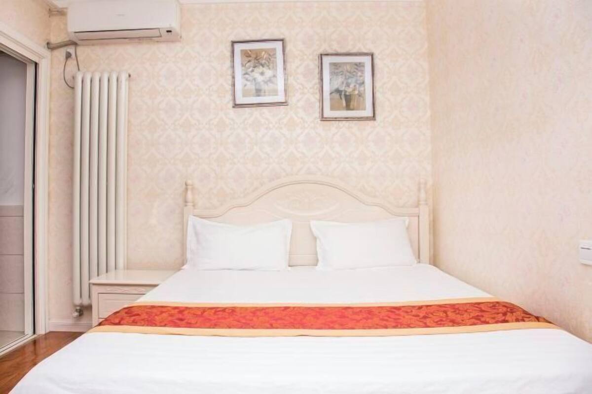 Ein Schlafzimmer mit einem Bett, einem Heizkörper und zwei gerahmten Bildern an der Wand.