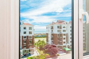 Vista desde una ventana de un edificio de varios pisos, con balcones, un patio con árboles y edificios distantes al fondo.