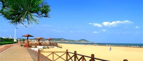 Un paseo marítimo de madera que conduce a una playa con sombrillas y una palmera.
