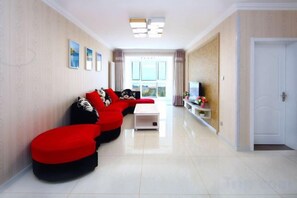 A modern living room with a sofa set, a coffee table, and a TV. - Qingdao Jinshatan Romantic Apartment (Qingdao)