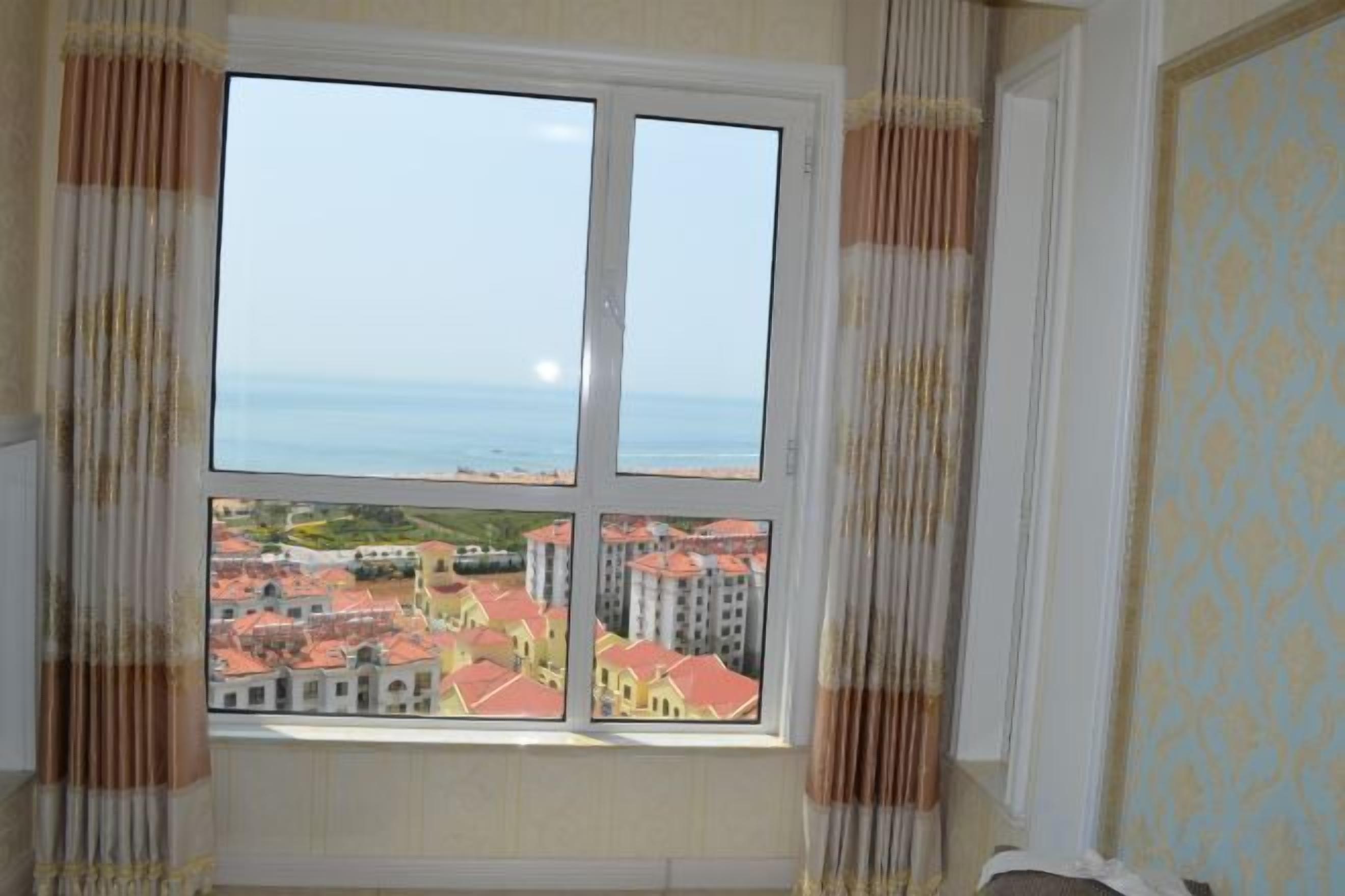 A room with a large window, curtains, and a view of buildings and water.