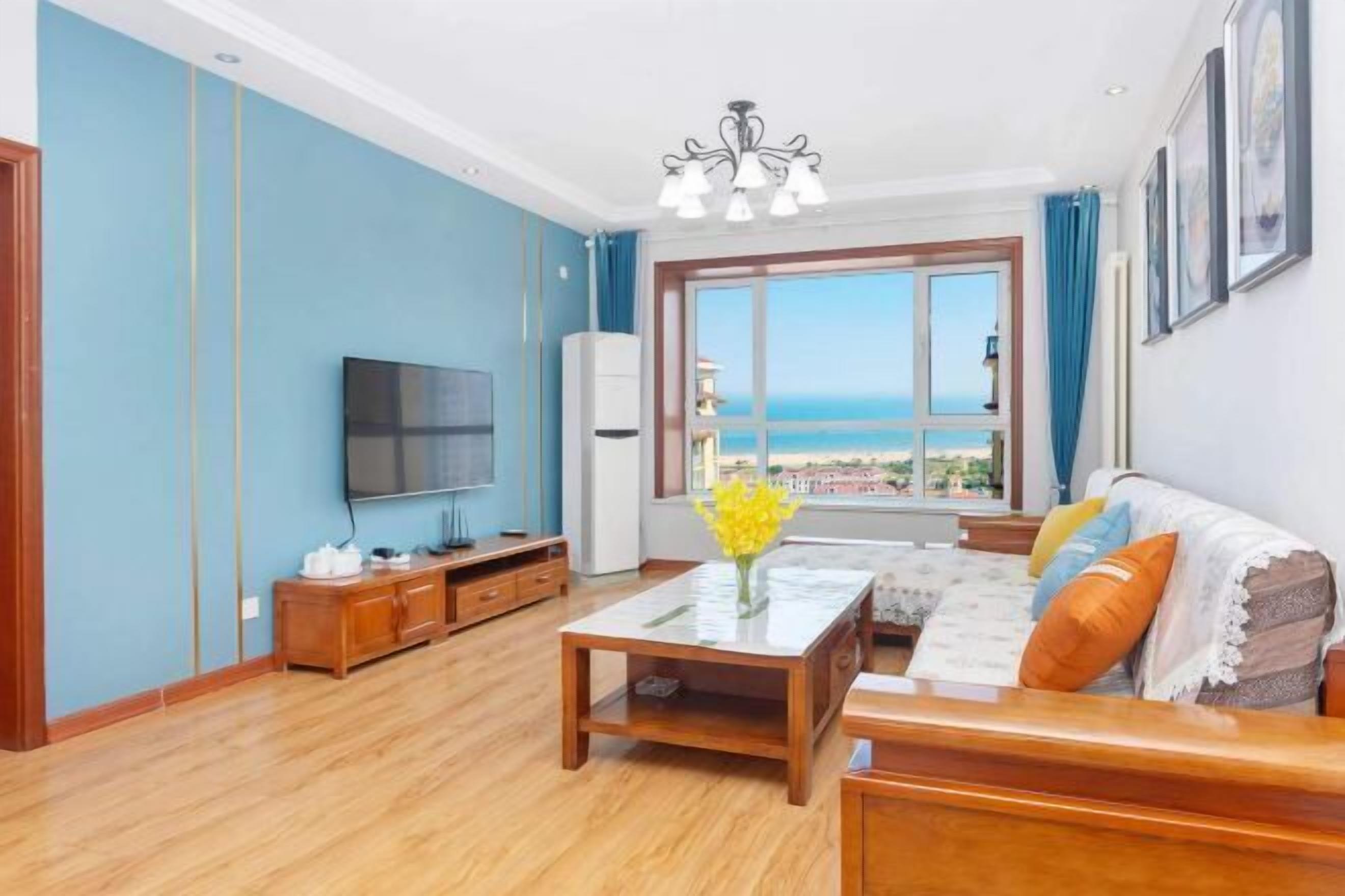 Una sala de estar con televisor, muebles de madera, un ventanal con vistas y una lámpara de araña.