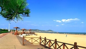 Een houten looppad dat naar een zandstrand leidt, met parasols en ligbedden.