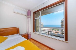 Una habitación de hotel con cama, ventana con vistas al mar y edificios, y una cortina.