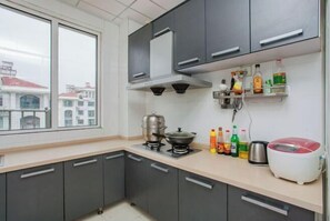 A kitchen with grey cabinets, a gas stove, a rice cooker, and a window with a view of buildings. - Qingdao Jinshatan Romantic Apartment (Qingdao)
