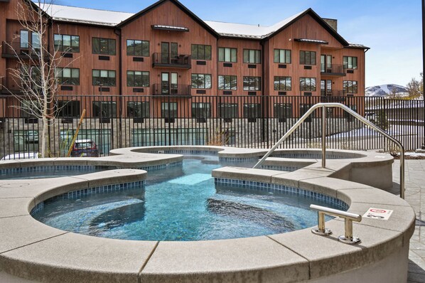 A modern building with a pool area, including a hot tub and a small pool, surrounded by a fence.