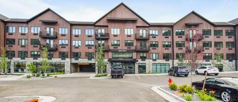A multi-story hotel with a modern design, featuring a central entrance, multiple balconies, and a parking area.