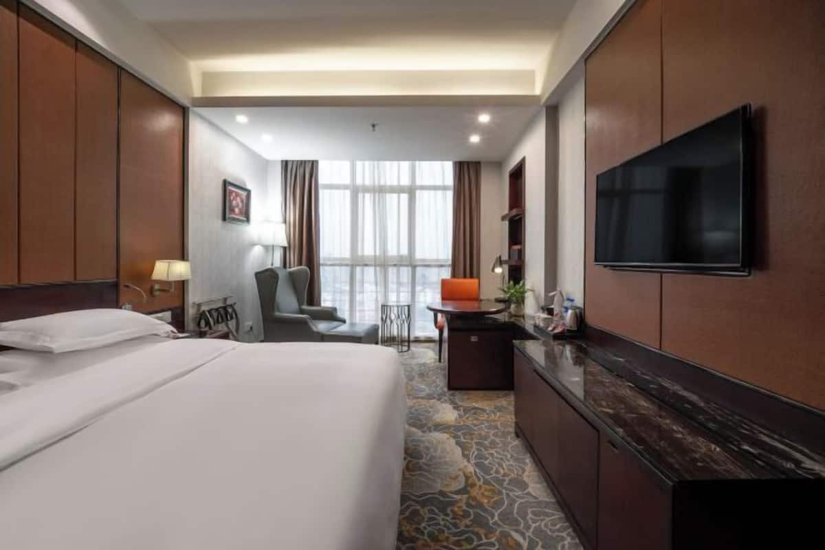 Habitación de hotel con cama, escritorio, silla, televisión y ventana con cortinas.