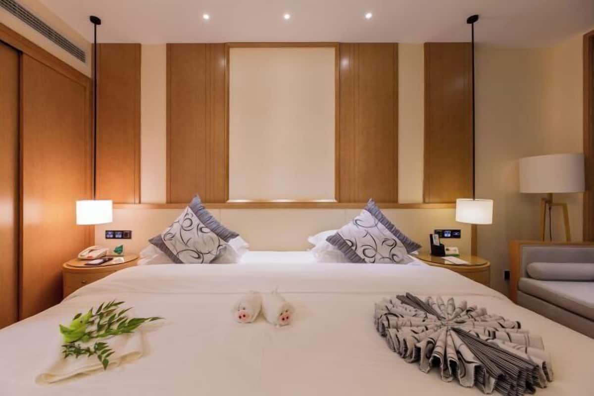 Habitación de hotel con una cama grande, dos mesitas de noche con lámparas, una silla y un ventanal.