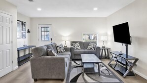 Ein Wohnzimmer mit grauem Sofa, Couchtisch, Fernseher auf einem Schrank und einem Beistelltisch mit Lampe.