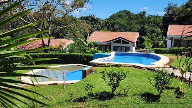 Un resort con piscina, vegetazione lussureggiante e ville dai tetti in tegole rosse.