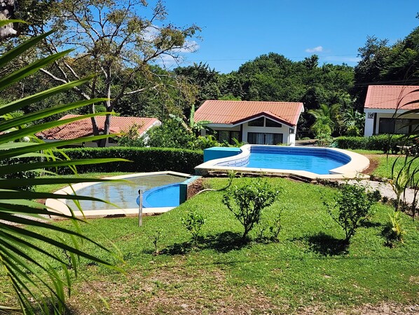 A resort with a swimming pool, lush greenery, and villas with red-tiled roofs.