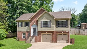 A two-story house with a brick facade, a front garage, and a well-maintained lawn. - Spacious 4-bedroom House near Downtown Clarksville (Clarksville)