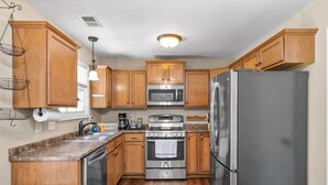 A compact kitchen with wooden cabinets, stainless steel appliances, and a granite countertop. - Spacious 4-bedroom House near Downtown Clarksville (Clarksville)