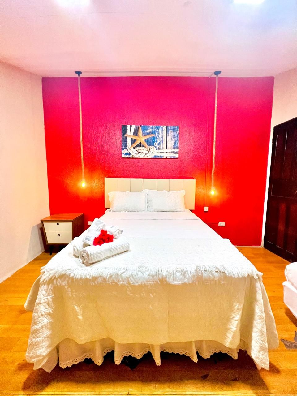 Una habitación de hotel con una cama grande, una mesita de noche, una obra de arte en la pared y una pared de acento roja.
