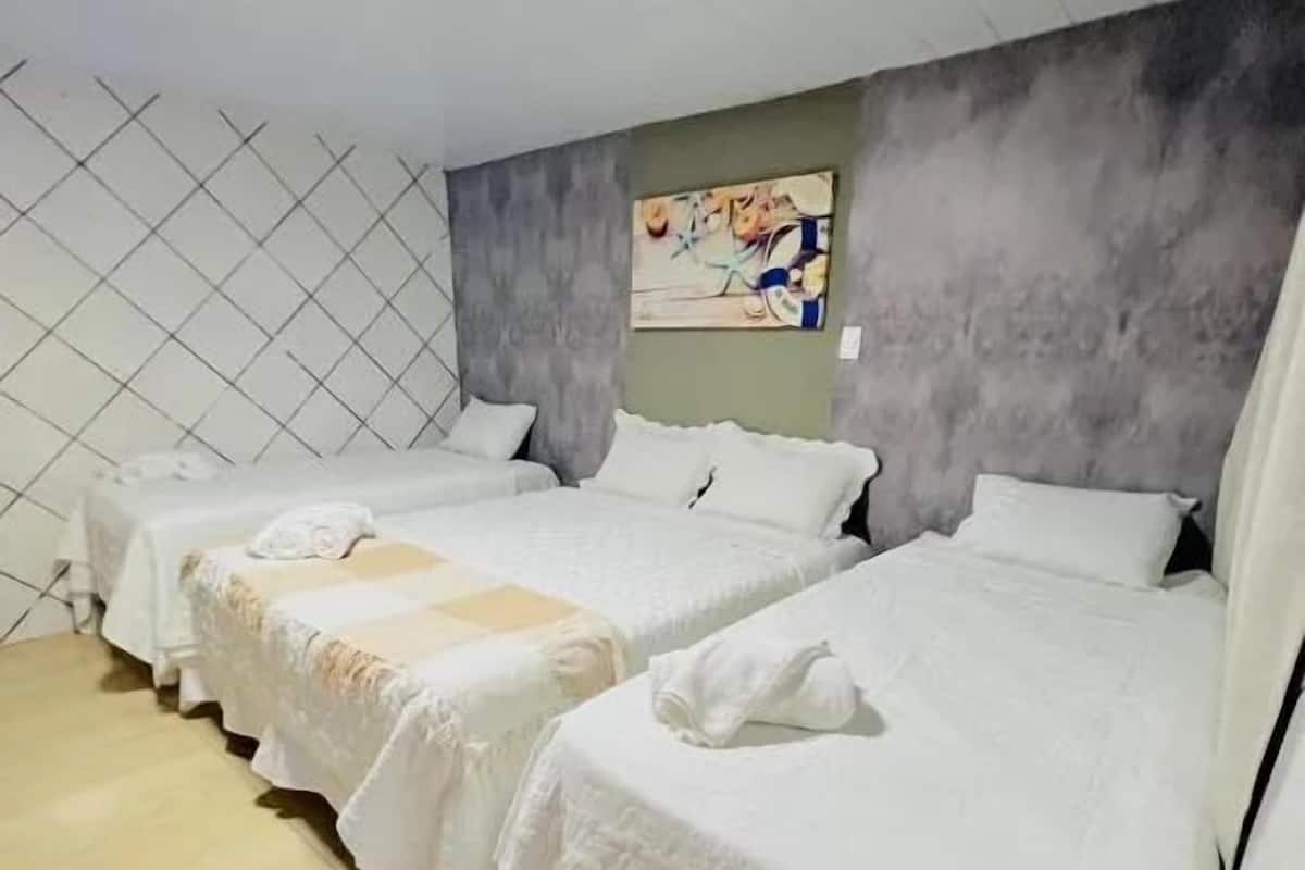 Ein Hotelzimmer mit drei Einzelbetten, einem gefliesten Boden, einer grauen Akzentwand und einem Gemälde über den Betten.