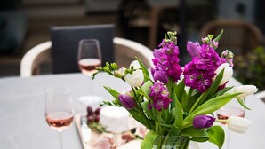 A dining table set with a vase of purple flowers, a cheese board, and wine glasses.