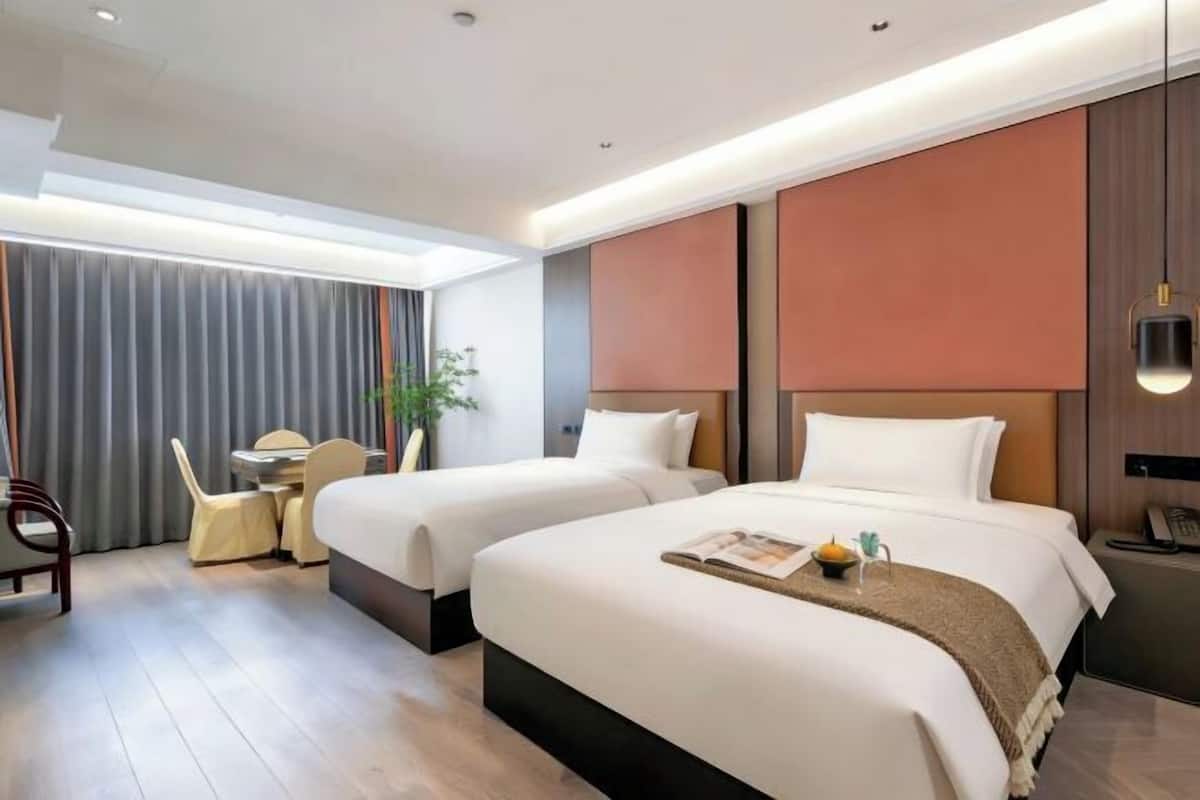 A hotel room with two beds, a desk, a chair, and a plant.