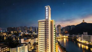Un hotel moderno de gran altura con un letrero llamativo, rodeado por un paisaje urbano y un río.