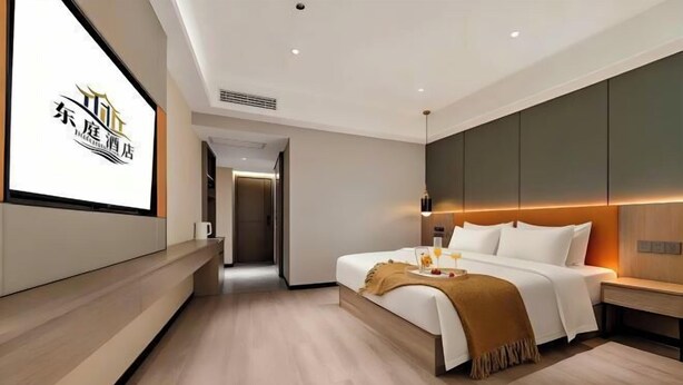 Una habitación de hotel moderna con una cama grande, una mesita de noche, un televisor montado en la pared y piso de madera.