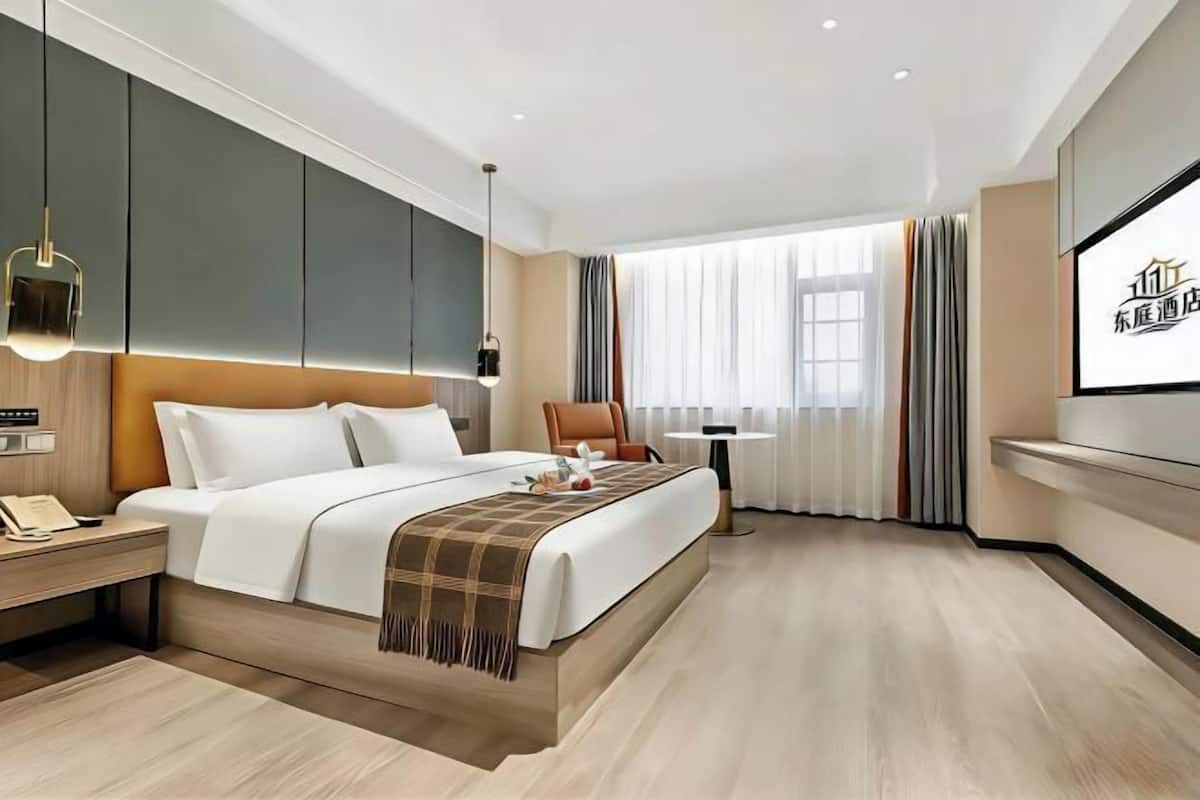 A modern hotel room with a large bed, bedside table, and a TV screen displaying hotel information.
