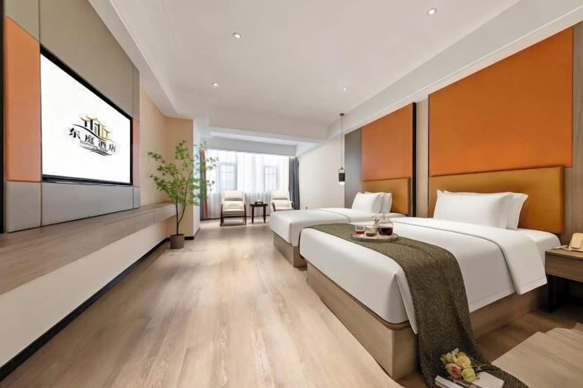 A hotel room with two beds, a TV, a plant, and a view of the outside.