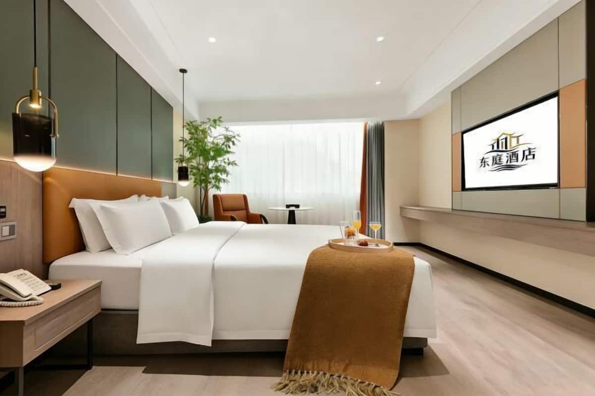 A modern hotel room with a bed, bedside table, lamp, and a TV screen displaying hotel branding.