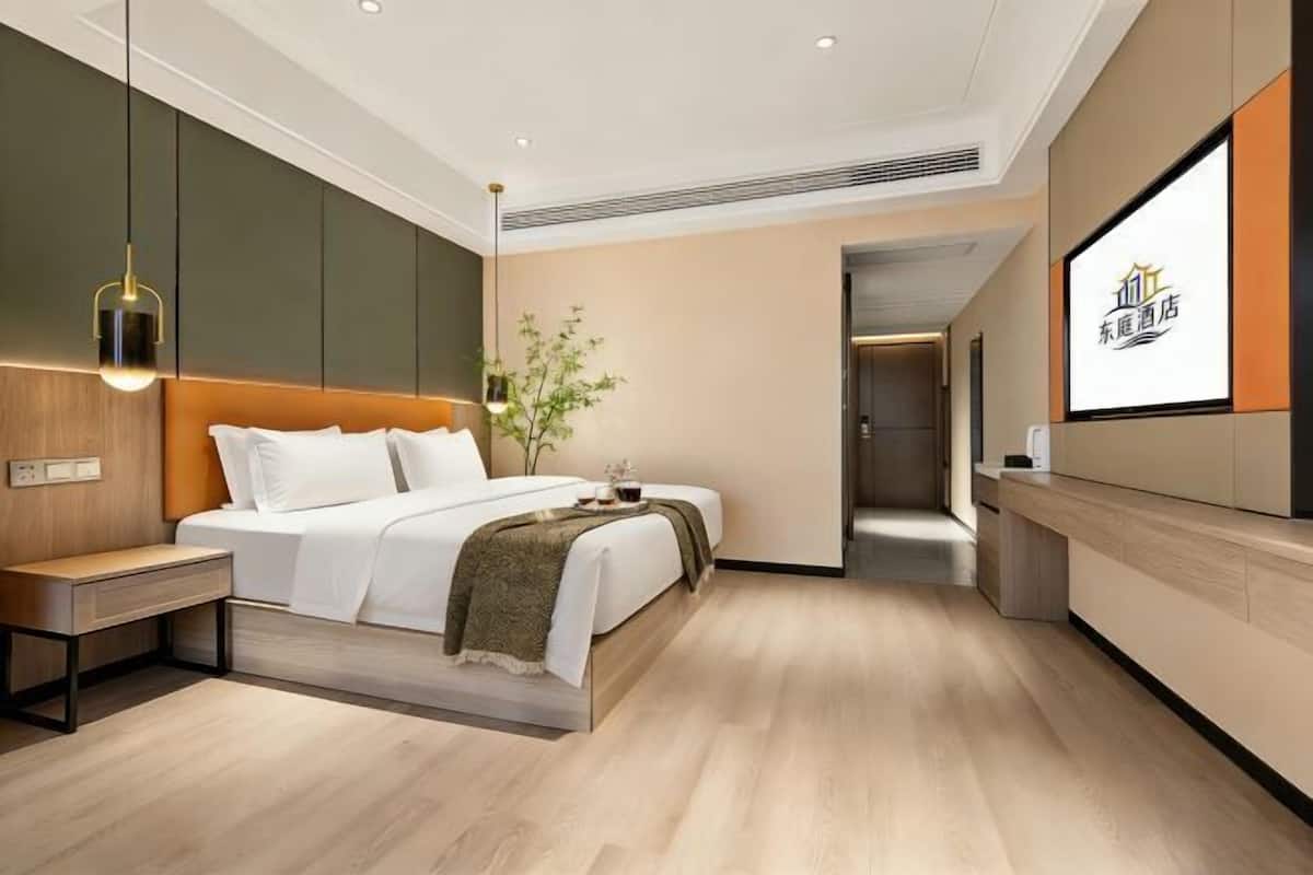 A modern hotel room with a bed, bedside table, and a large window.