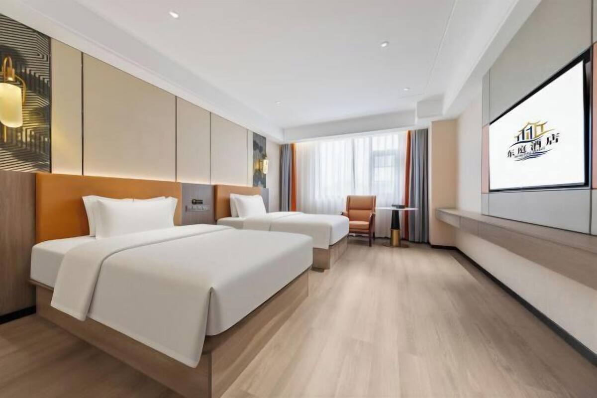A hotel room with two beds, a small table, and a chair.