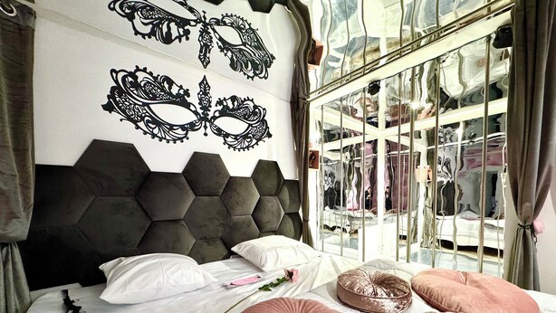 Un dormitorio con cabecera hexagonal, cama con muchos almohadones y un espejo grande de marco ondulado.