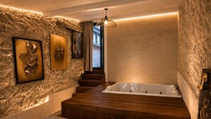 A modern bathroom with a stone wall, a wooden bench, a bathtub, and a hanging light fixture. - Caporizon-love House-une Maison Entiere Dédiée aux Plaisirs de L'amour (Biras)