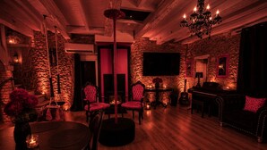 A dimly lit room with a stone wall, a fireplace, a chandelier, and a piano. - Caporizon-love House-une Maison Entiere Dédiée aux Plaisirs de L'amour (Biras)