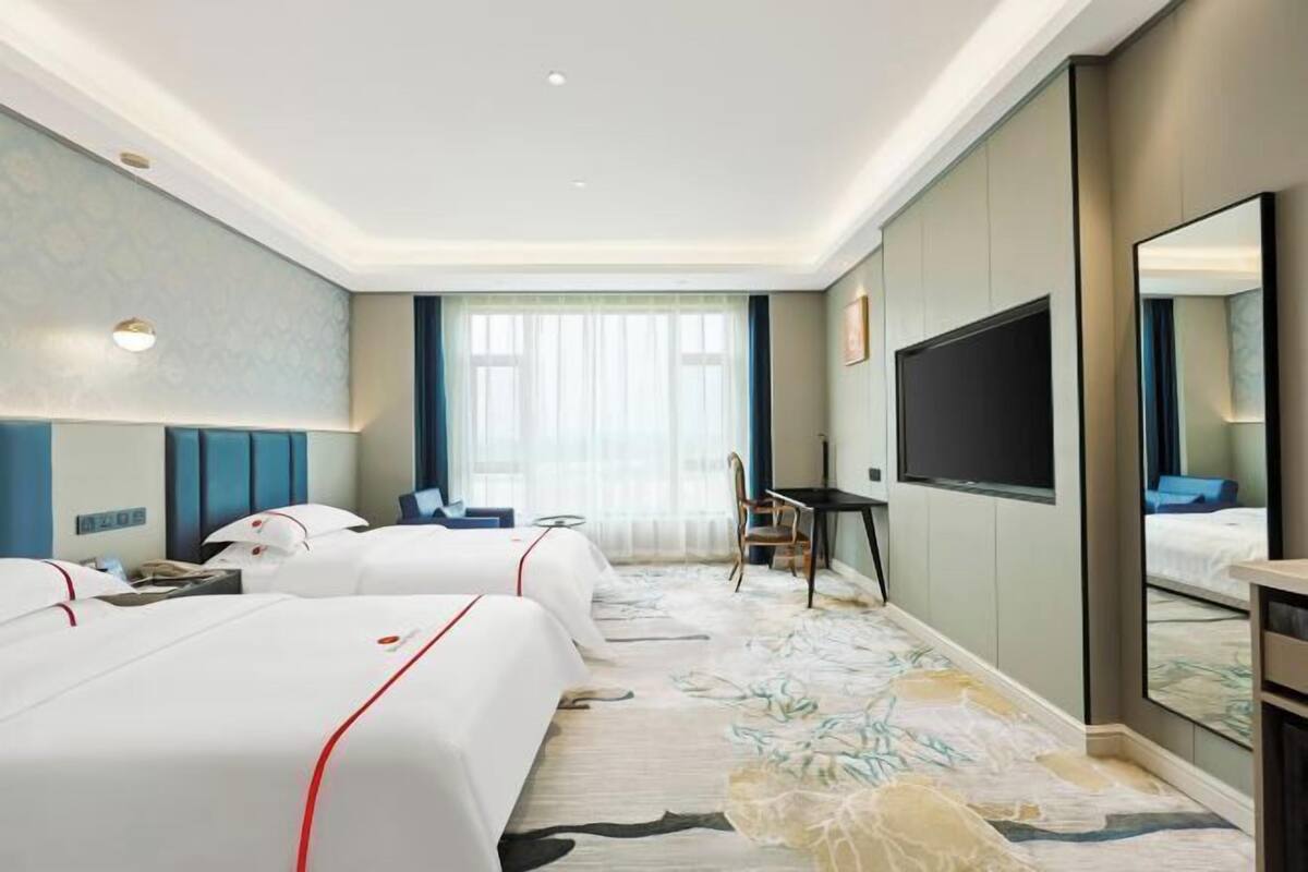Une chambre d’hôtel avec deux lits, un bureau, une chaise, une télévision et un grand miroir.