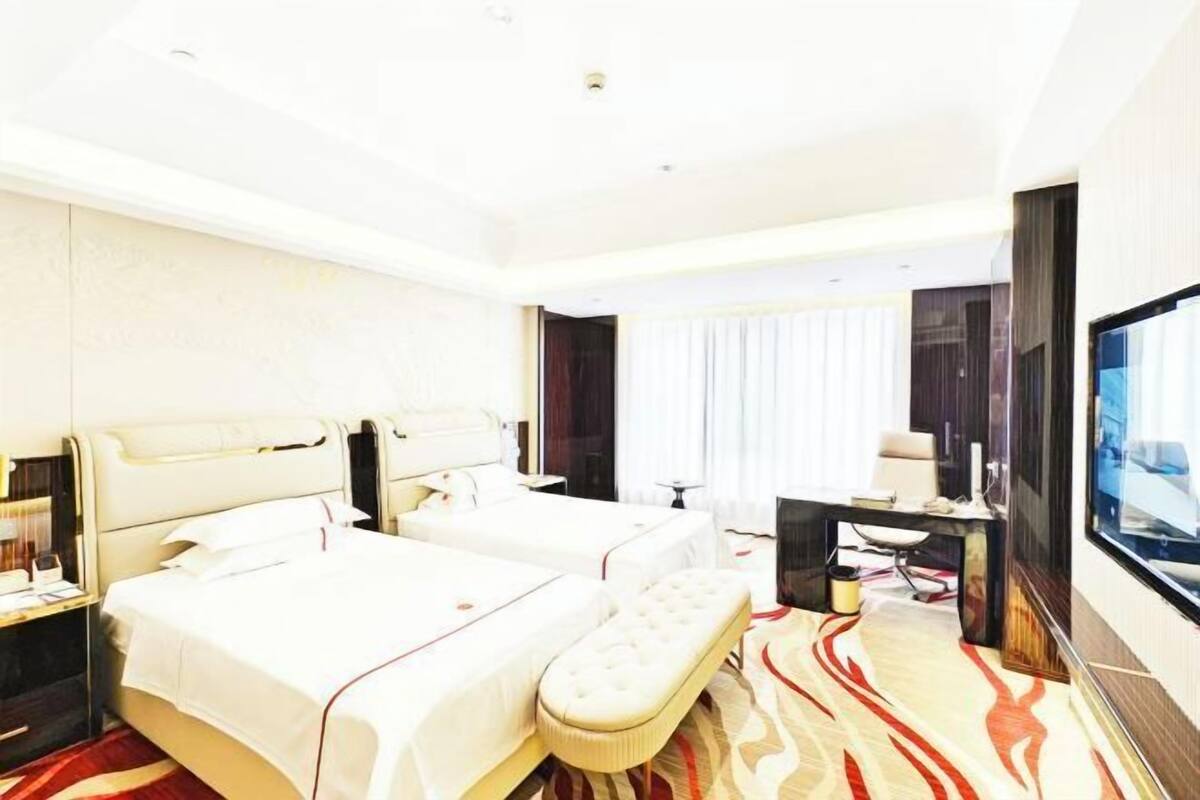 Une chambre d’hôtel avec deux lits, un bureau, une télévision et une grande fenêtre.