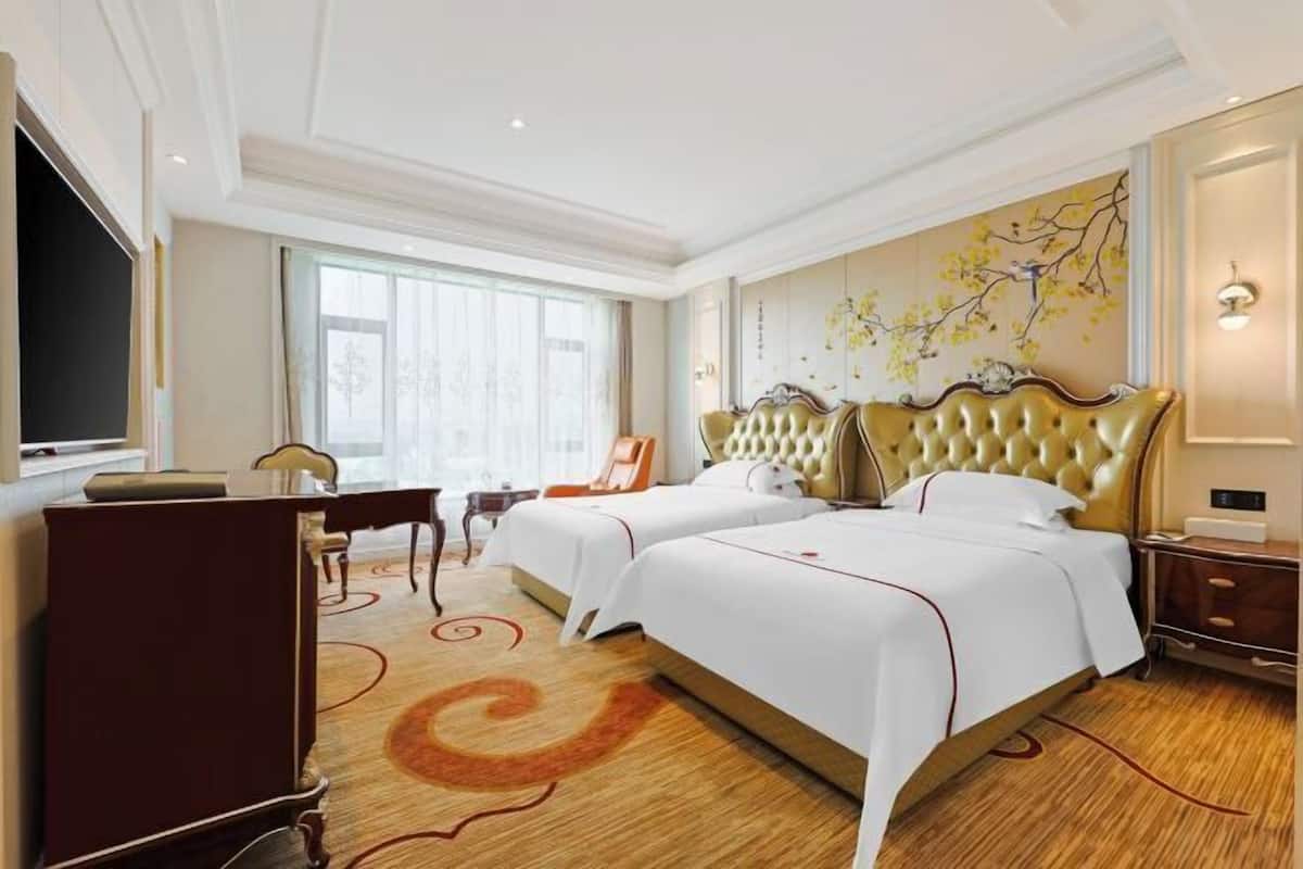 Une chambre d’hôtel avec deux lits, un bureau, une chaise et une grande fenêtre.