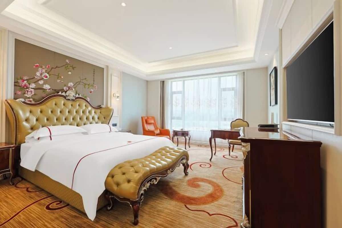Une chambre d’hôtel avec un grand lit, un bureau, une chaise, une télévision et une fenêtre.