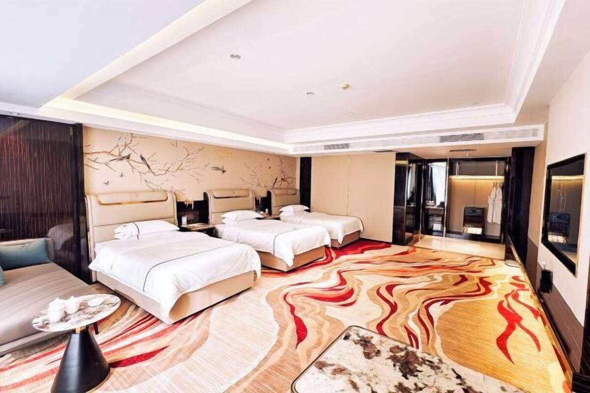Une chambre d’hôtel avec deux lits, un canapé, une table à manger et une grande moquette à motifs.