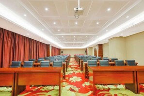 A conference room with rows of tables and chairs, a large screen at the front, and a red curtain backdrop. - Baiyun International Hotel (Huadian)