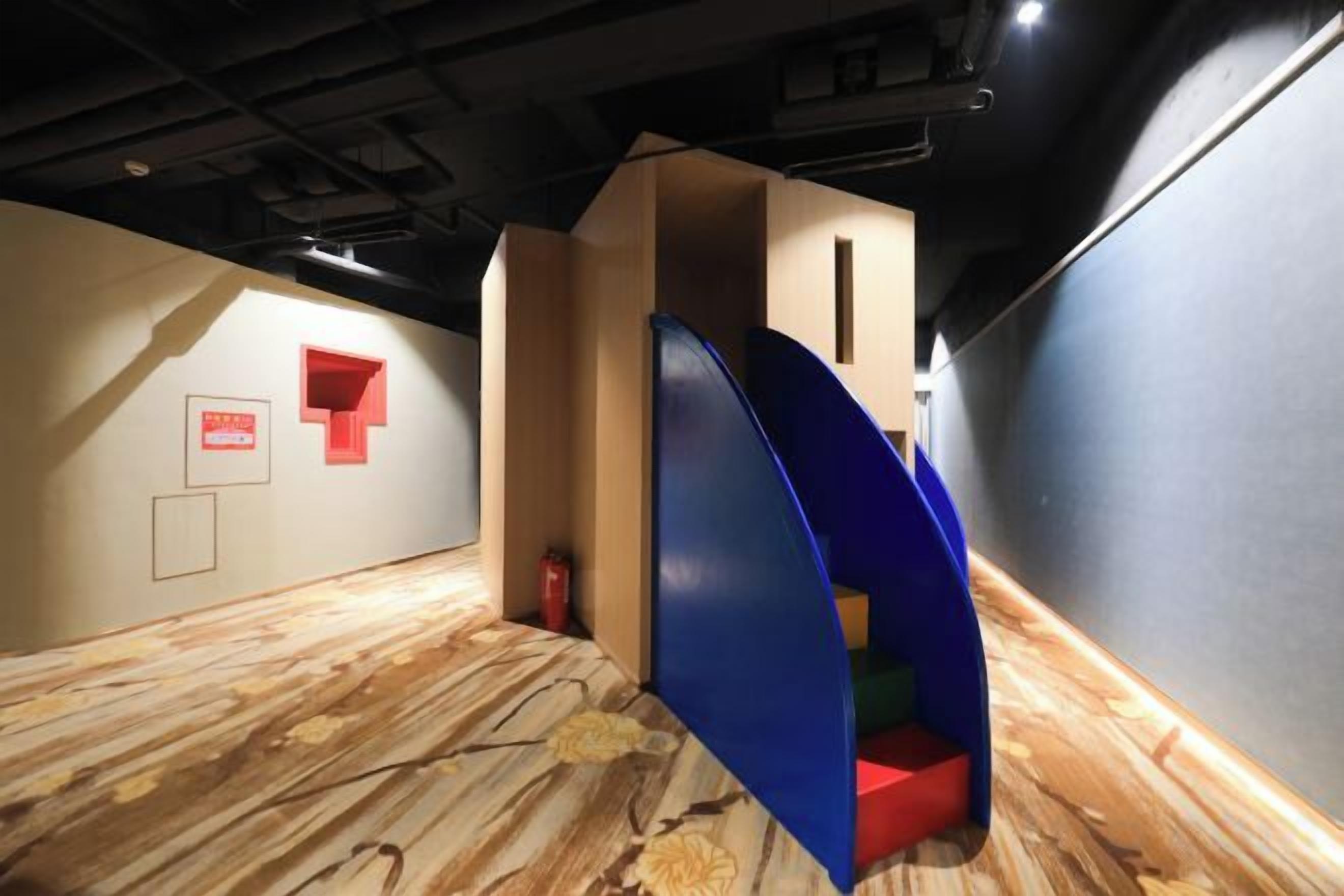 Una habitación con suelo de madera, una estructura de juego azul y roja, y un letrero rojo en la pared.