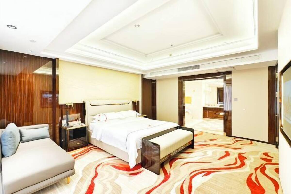 Une chambre d’hôtel avec un lit, un canapé, une table de chevet et un miroir.